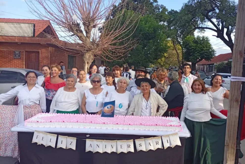Vecinos que participan de los ballets folclóricos frente a la torta de aniversario
