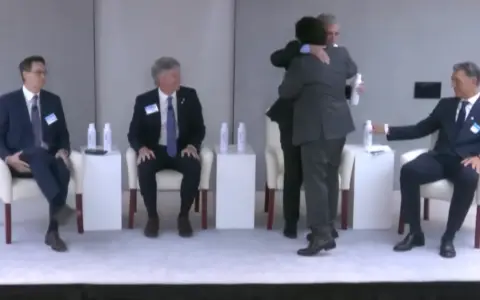 Gustavo Sáenz, cruzó al panel y rompió el protocolo de un acto ya empezado para capturar el abrazo con Caputo.