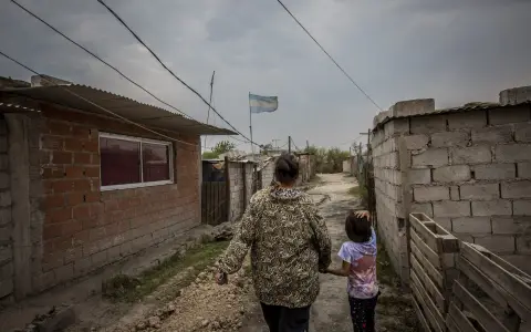 Una madre y su hija caminan entre calles de tierra y viviendas precarias, donde la pobreza también se mide en servicios ausentes.